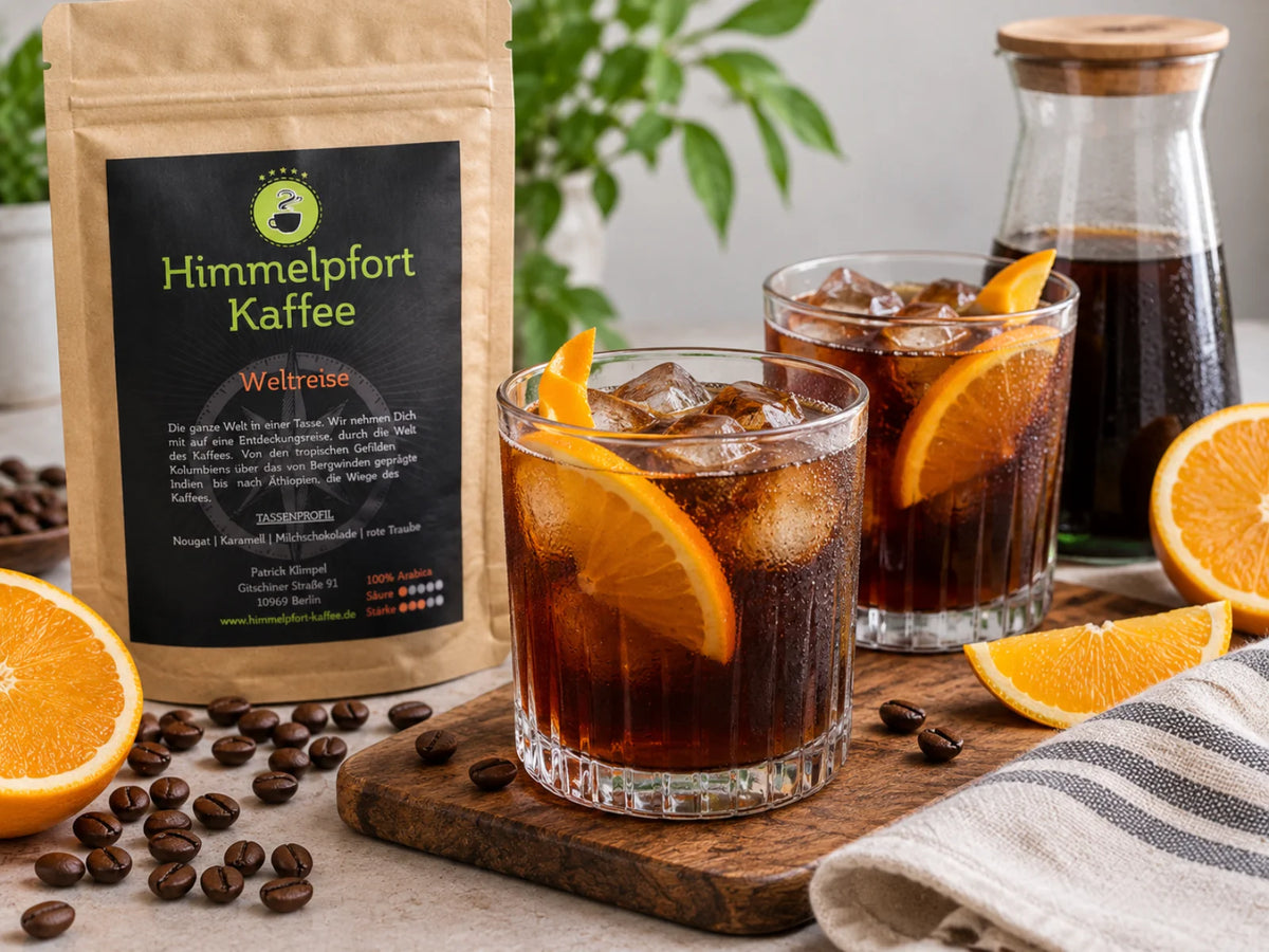 Cold Brew mit Weltreise, Eiswürfeln und frischer Orangenschale in zwei Gläsern, daneben die originale Himmelpfort-Kaffee-Tüte Weltreise, eine Karaffe Cold Brew, Orangenscheiben und Kaffeebohnen