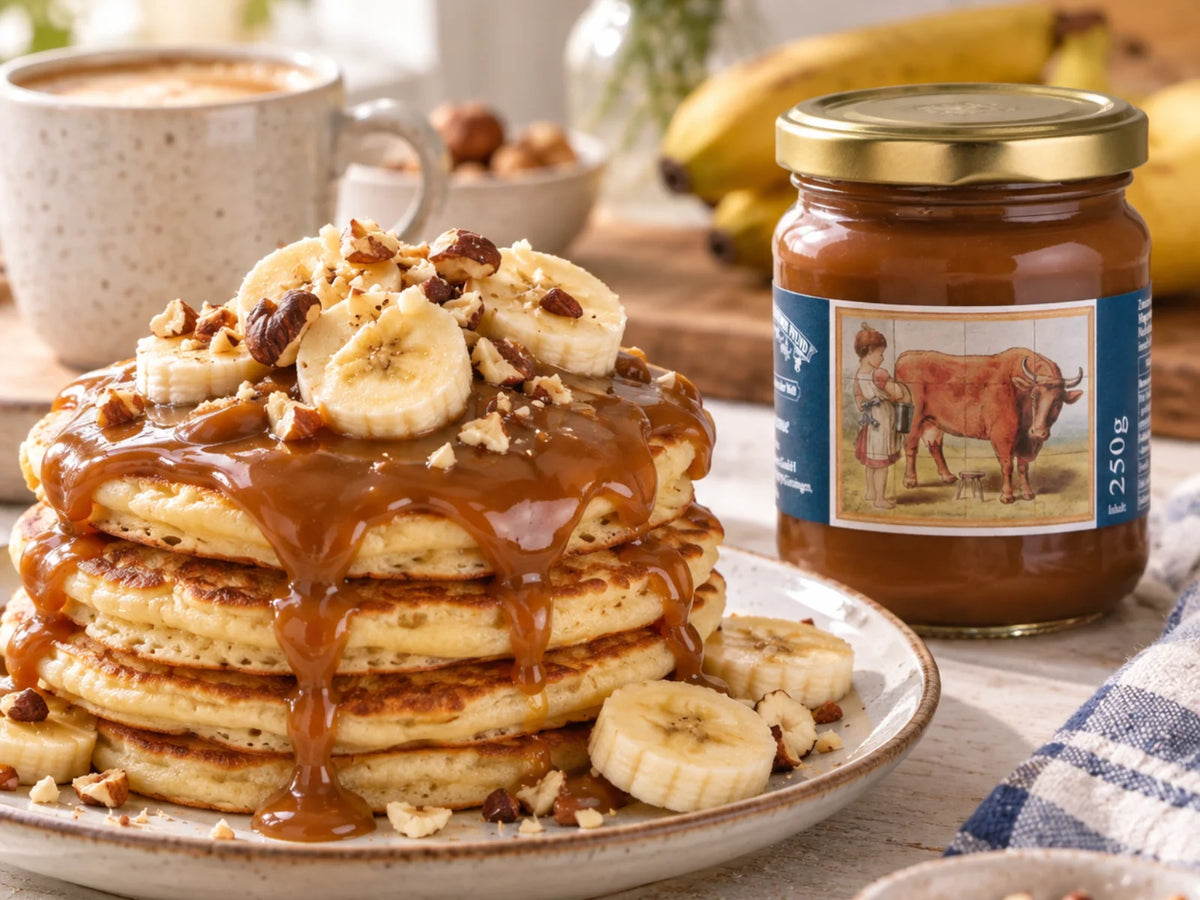 Fluffige Pancakes mit Confiture de lait, Bananenscheiben und gehackten Haselnüssen, daneben das Originalglas der Pfunds Milchkaramellcreme