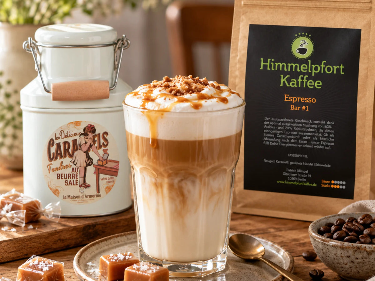 Gesalzener Karamell-Latte in einem Glas, dekoriert mit Sahne und Karamell, daneben die originale Karamell-Süßigkeitendose und eine Packung Himmelpfort Kaffee Espresso Bar #1 auf hellem Untergrund.